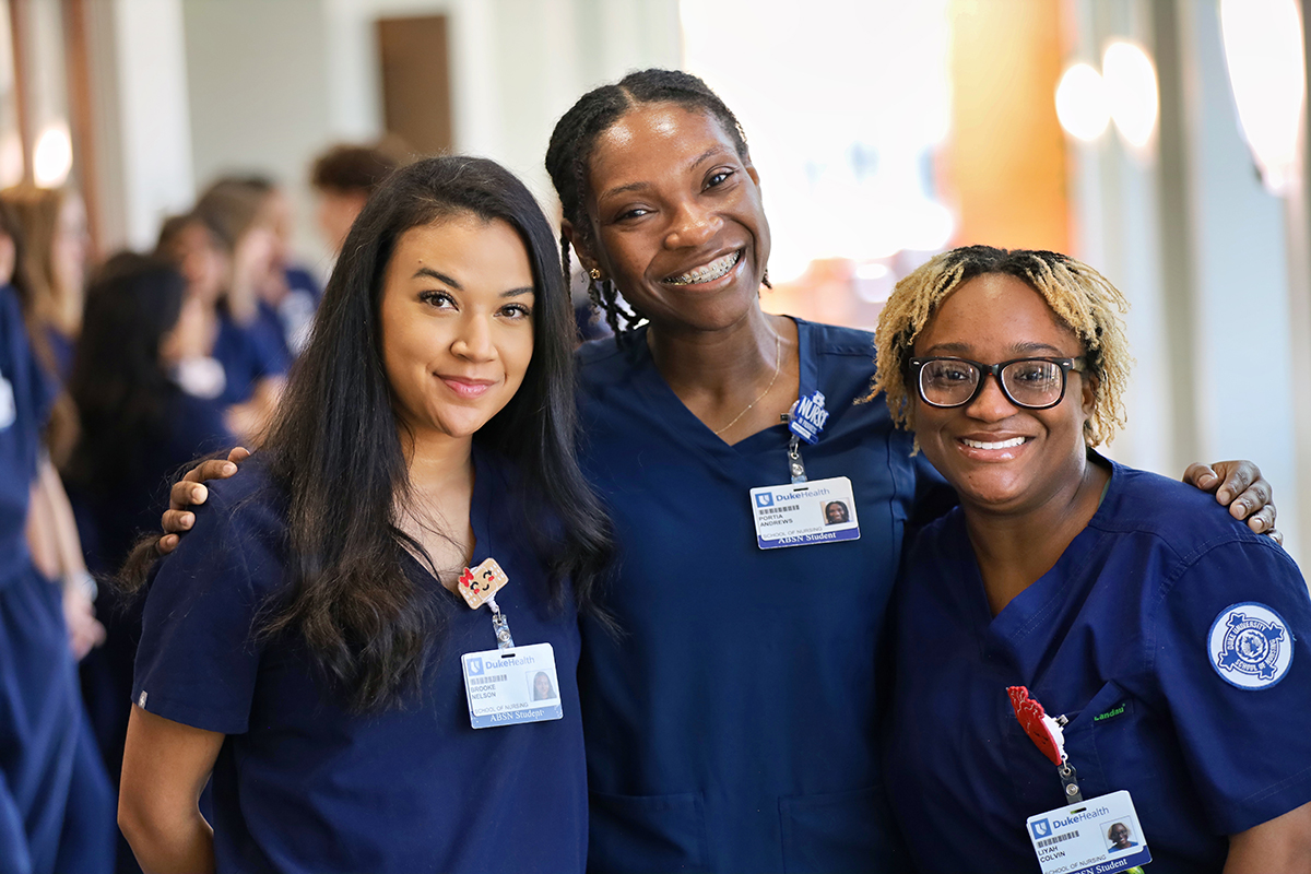Three students in scrubs standing together and smiling