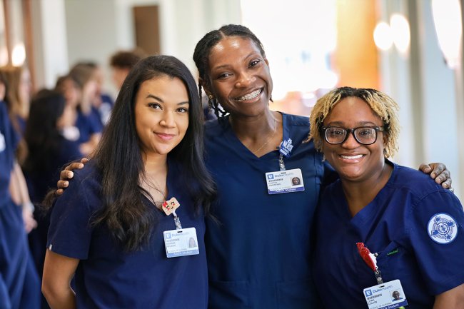 Three students in scrubs standing together and smiling