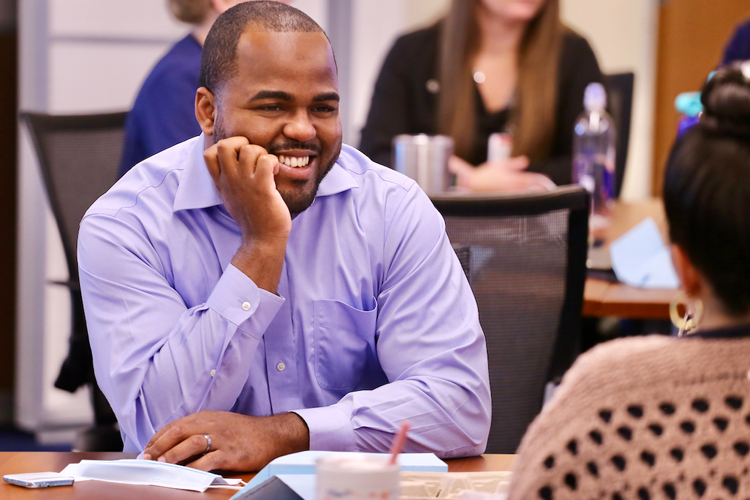 A Duke University School of Nursing Psychiatric Mental Health Care student is smiling among other students in a large classroom setting.