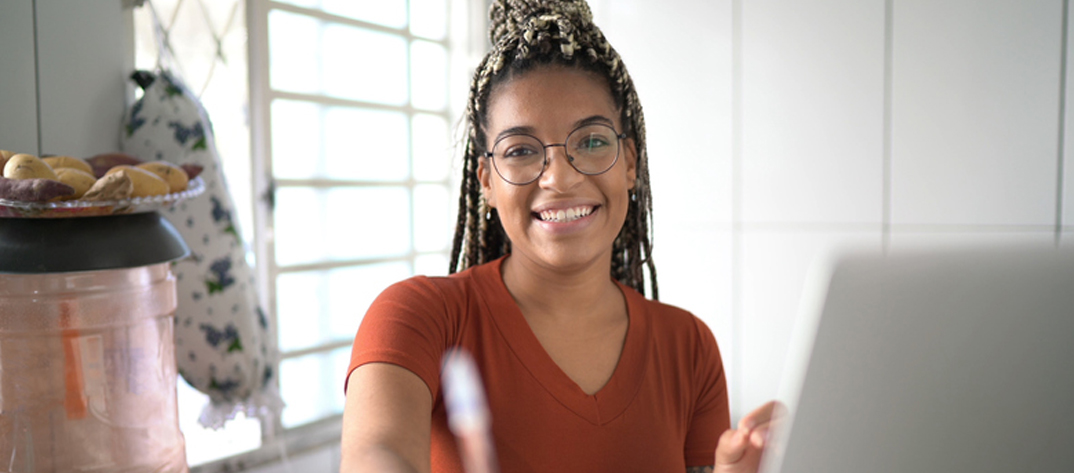 A Duke nursing student learning from a home environment sits in front of a laptop with a pencil in her hand and smiles.